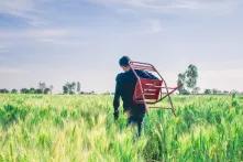 man in black sweater carrying chair in middle of field