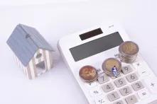 Miniature businessman sitiing on 2 euro coins and calculator and house