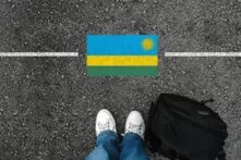A man with a shoes and backpack is standing on asphalt next to flag of Rwanda and border