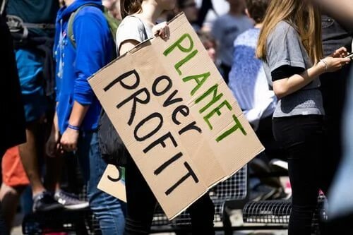 woman holding planet over profit placard