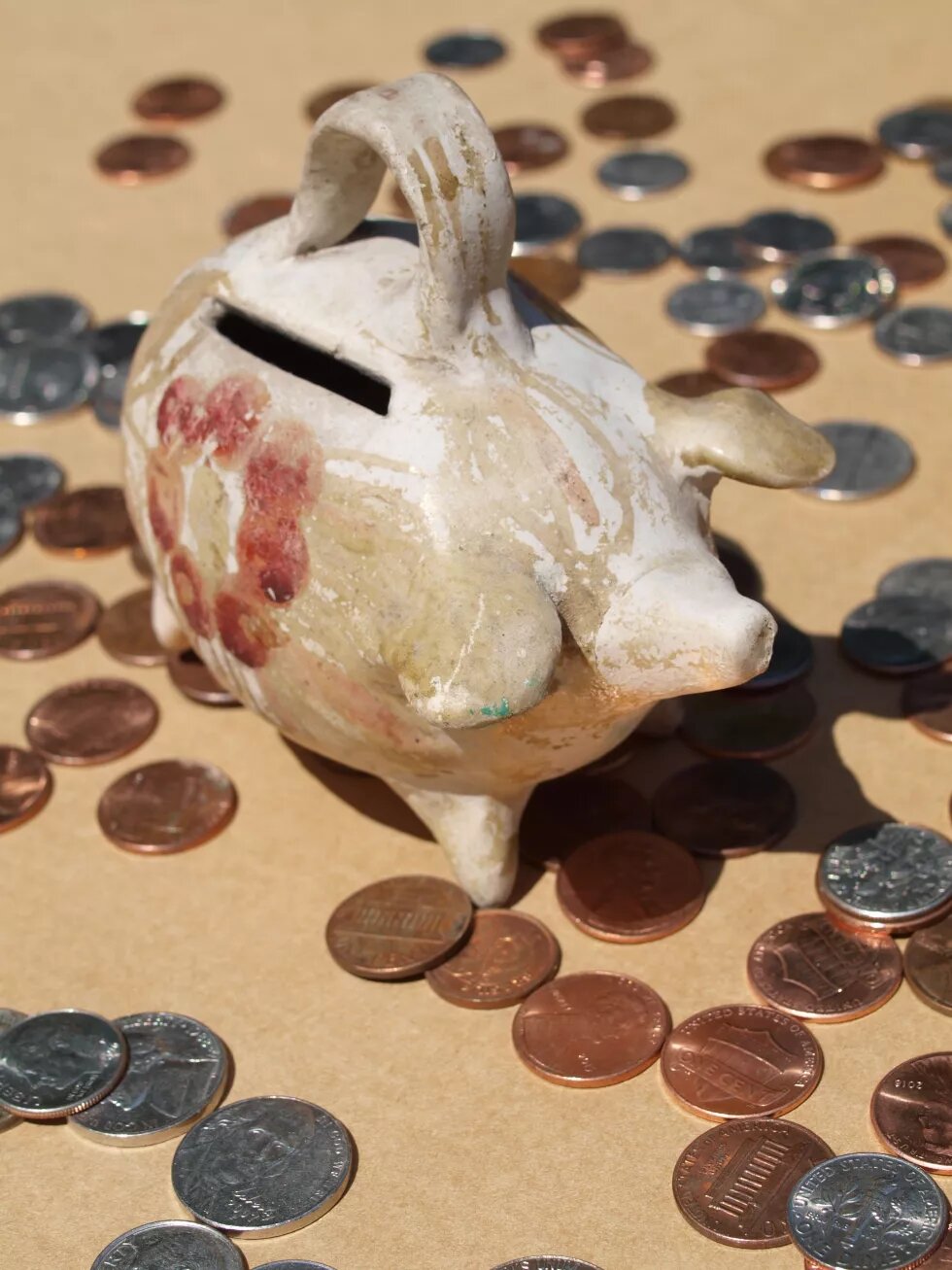 Vintage 1960s potter piggy bank from South America with scattered American coins on a brown background.