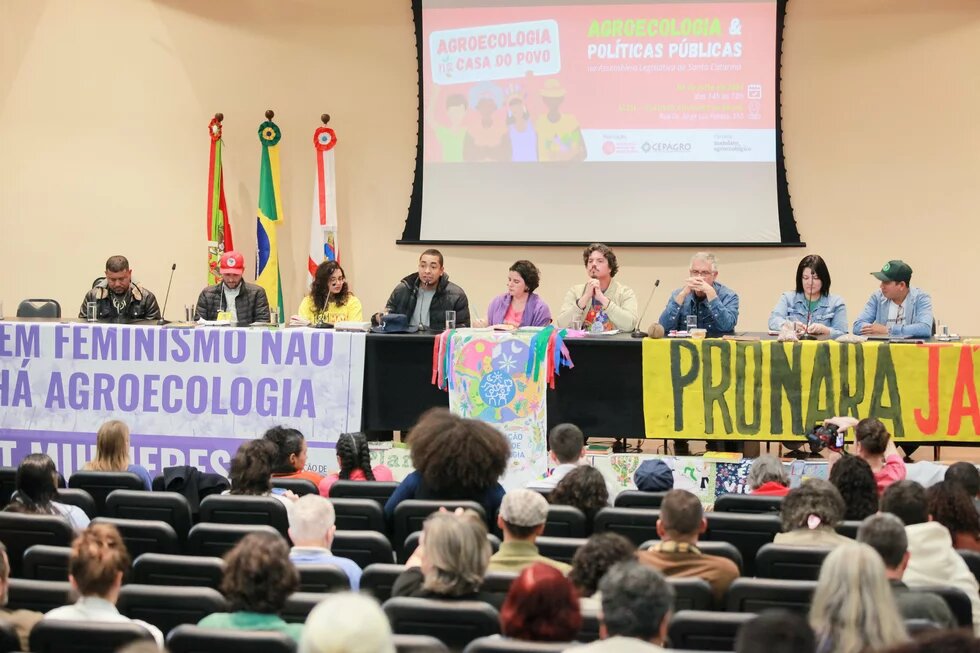 Photo: A discussion during an event on agroecology and public policies. People are seated at a table with banners in the background.