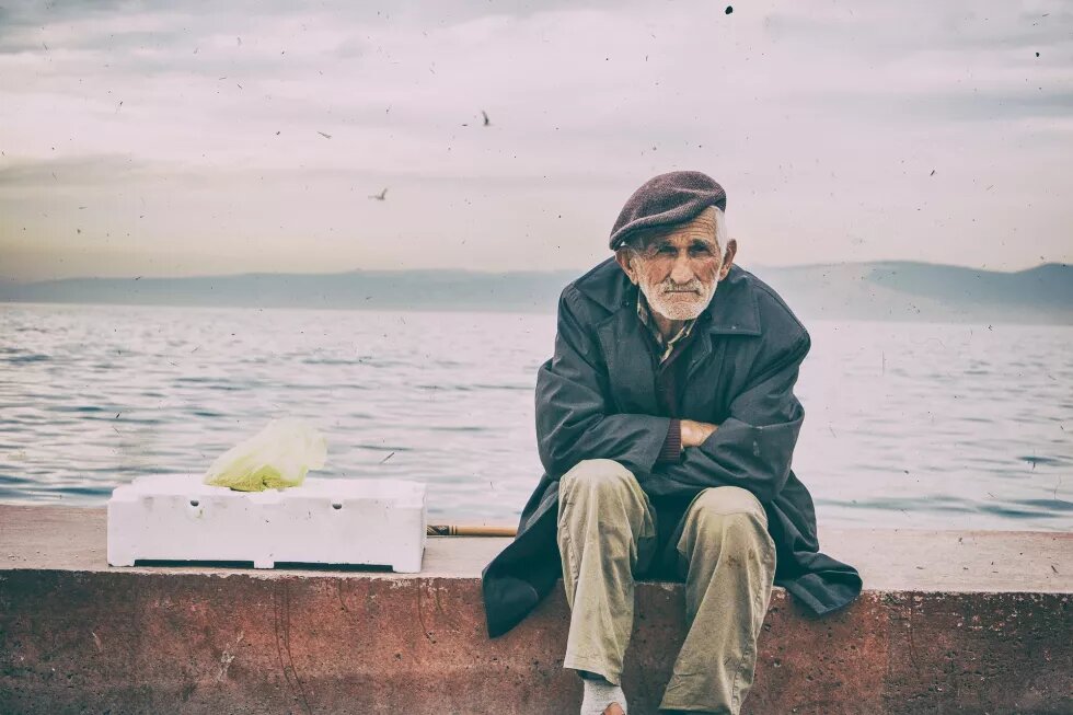 Europa? War da was? Europa? War da was? - Ein alter Mann sitzt auf einer Mauer am Meer